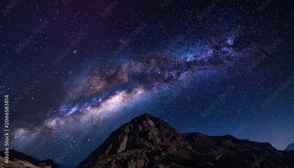 Fototapeta premium The Milky Way arches majestically over a rugged mountain peak under a sky full of stars.