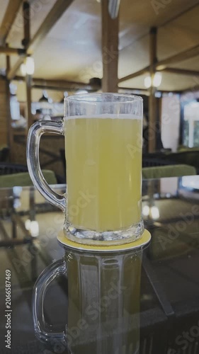 Close up of a refreshing glass of light beer on a coaster. The mug sits on a reflective table in a dimly lit bar or restaurant