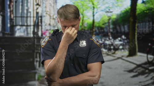 Foto Police officer man pinches nose by visible badge on street with folded arms and navy uniform shirt; stress reflection