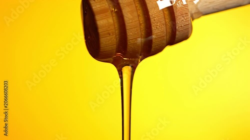 Liquid honey falling from dipper on yellow.