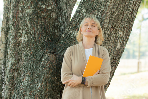 Dream and hope concept, old woman holding book and relax with close eye to think and dreaming under tree in park