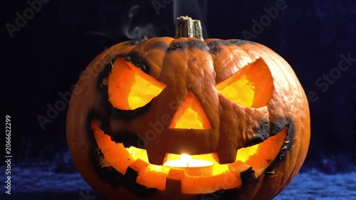 Lit carved pumpkin with spooky smoke and glowing eyes for halloween festivities and autumn seasonal decor themes in a dark and moody atmosphere