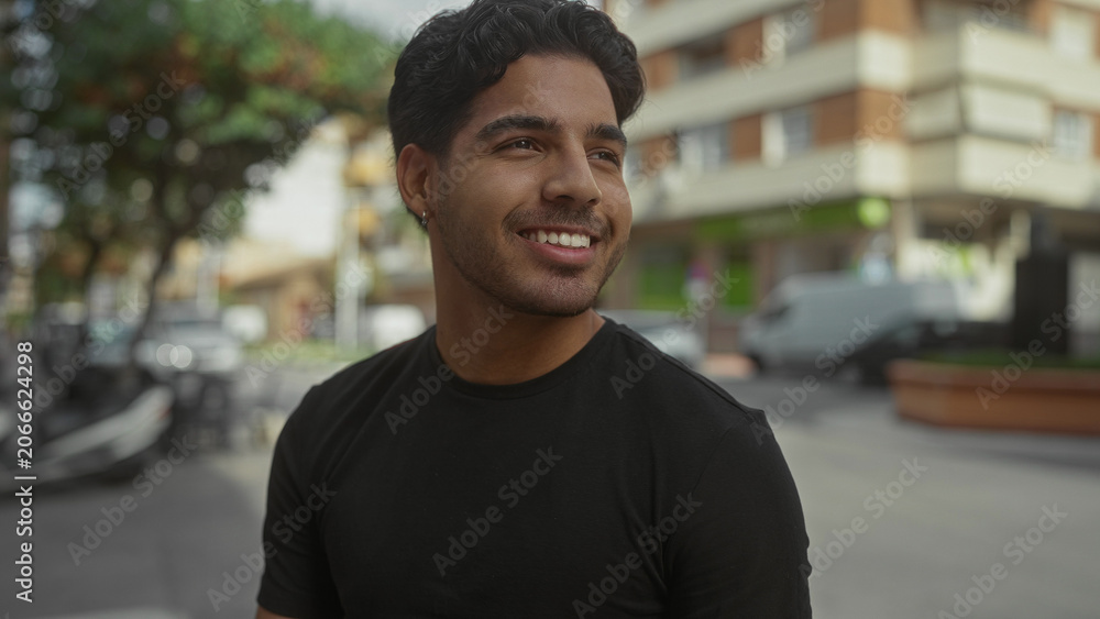 Fototapeta premium Man smiling with visible earring and teeth, head turned to side while standing on a busy street with scooters and buildings in view; carefree joy.