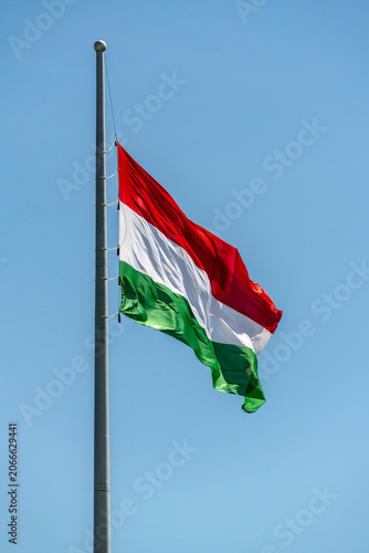 Hungarian flag waving on a flagpole against a clear blue sky during a sunny day