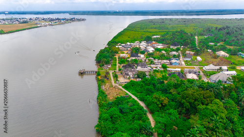 Aerial view of a riverine village nestled along the banks of a wide river, surrounded by lush green vegetation and palm trees in Rivers, Nigeria.