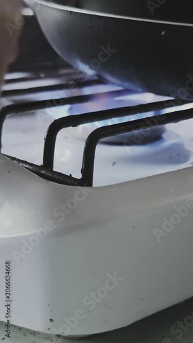 Detailed close up view of a person's hand lighting a gas stove. A black pan sits on the burner as the blue flame ignites for cooking
