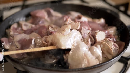 Raw chicken livers are tossed with a wooden spatula in a hot cast iron skillet on a kitchen stove. Concept of traditional cooking, poultry preparation, and nutritious offal recipes.