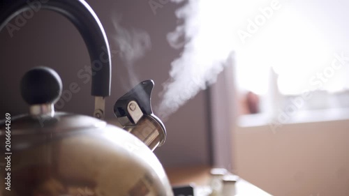 A stainless steel whistling kettle boils water on a kitchen stove while thick white steam rises from the spout. Concept of morning routine, tea preparation, and domestic comfort.