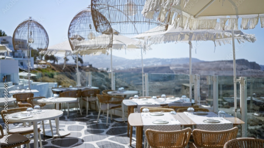 Fototapeta premium Sunlit terrace dining scene softly blurred with shallow bokeh and defocused coastal view, cafe; background backdrop copyspace calm.