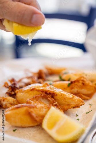 Bild auf Leinwand Hand squeezing fresh lemon juice over fried calamari squid in a Greek tavern