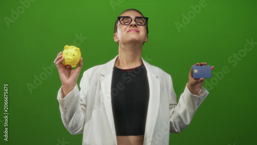 Photos Woman holding a yellow piggy bank and a blue creditcard while smiling with closed eyes in studio; financial confidence