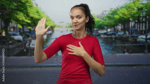 Canvastavla Woman with raised right hand and left hand on chest on street making oath pledge gesture in front of canal and bridge; sincerity apology