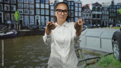 Photography Woman in white shirt and glasses beckons with hands by a canal on a street; urban invitation interaction
