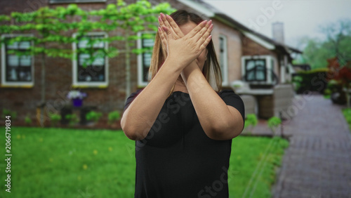 Bild auf Leinwand Woman with hands crossed over face at building entrance showing hands and fingers in a black shirt; privacy silence