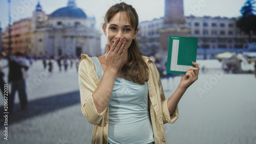 Billede på lærred Woman holds green learner l sign, bare shoulder visible at building in st peter's square; confidence learning travel