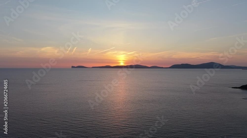 Aerial view of Capo Caccia at sunset with slow drone descent toward sea level showing dramatic cliffs and Mediterranean sea in golden light.