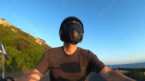 Slow motion POV selfie of biker leaning through coastal curves at sunset with sea views warm golden light and scenic Mediterranean road in Sardinia.