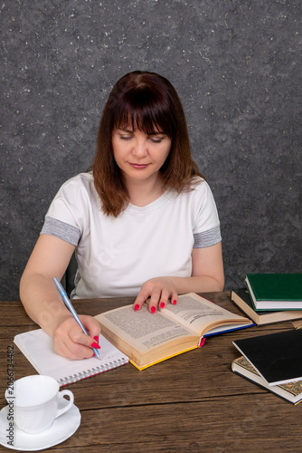 A woman takes notes at her desk while reading a book and studying