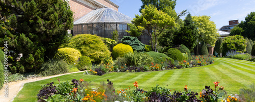 Sunlit Herbgarden (Kruidtuin) in Leuven, Belgium with historic greenhouse, formal lawn and colorful flower beds
