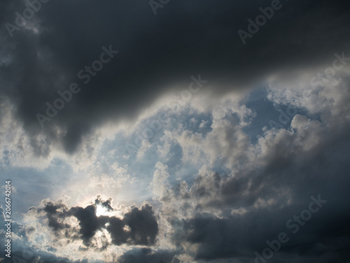 Dark thick clouds that partially obscure the bright sun twilight rays sunlight penetrating through clouds stormy weather or afternoon skies.
