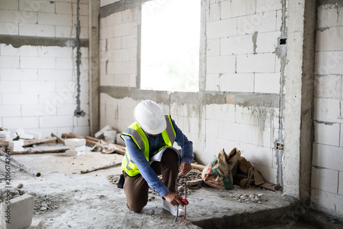 Construction engineer reviewing blueprints and measuring wall alignment inside a building.