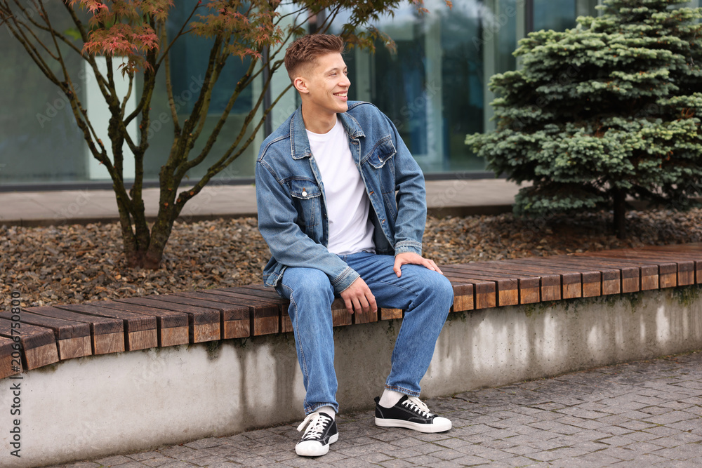Fototapeta premium Young man in stylish denim outfit on bench outdoors