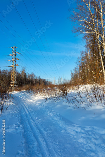 High voltage power lines and towers stretching across a snowy winter landscape with forest. Electricity transmission and power grid infrastructure.