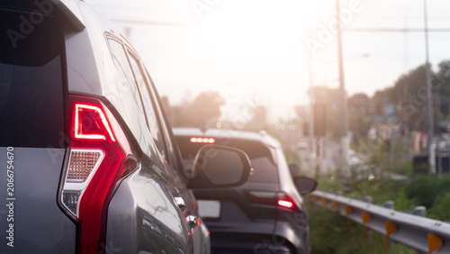 Vehicles are gridlocked in a heavy urban traffic jam during a bright afternoon. A silver SUV's glowing red tail light assembly stands out sharply in the foreground lane.