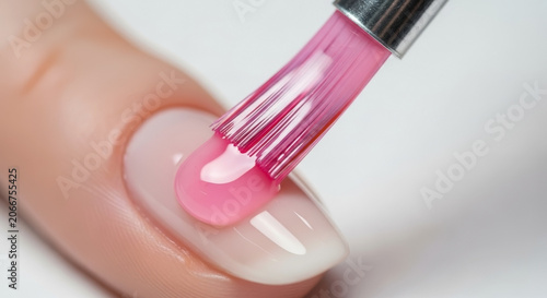 Close up of female finger with natural nail, applying gel polish using professional brush. Brush delicately spreads shiny pink substance, applying gel polish for perfect smooth finish.