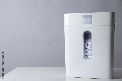 Shredder with cut paper pieces on white table against grey background. Space for text