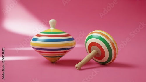   
Two colorful wooden spinning tops with striped patterns placed on pink surface vibrant nostalgic childhood toy leisure design concept