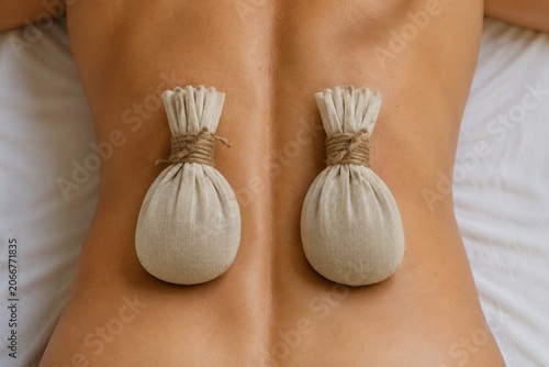 Woman receiving herbal bolus massage. Alternative medicine therapy on back for muscle relaxation. Spa treatment with organic compresses for healing and body care in wellness center.