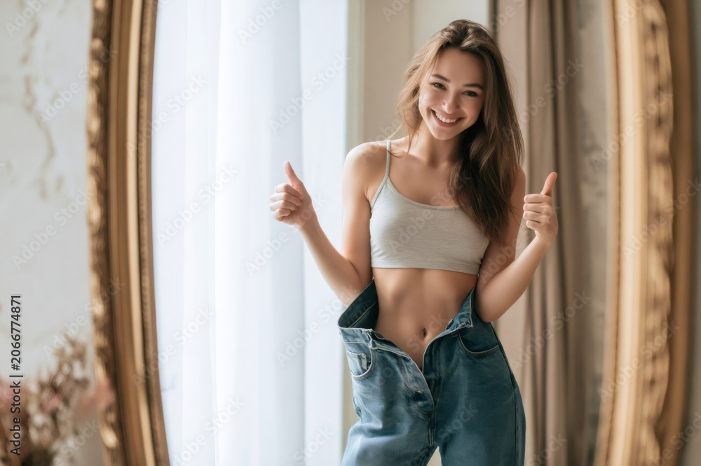 Fototapeta premium Young woman showing weight loss success with thumbs up