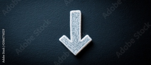 Close-up of white downward arrow on dark textured background, symbolizing decline or decrease
