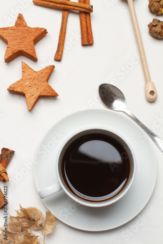 Una taza de cafe junto a unas ramsa de canela y unas estrellas de decoracion de madera sobre un fondo blanco. Vista superior y de cerca. Formato vertical