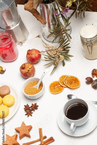 Una taza de cafe junto a un plato con macarons, unas granadas, rodajsa de naranja sobre un fondo blanco. Vista superior y de cerca. Estilo bodegon