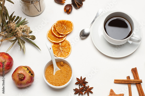 Una taza de cafe junto a unas granadas, rodajas de naranjas y ramas de canela sobre un fondo blanco. Vista superior y de cerca. 