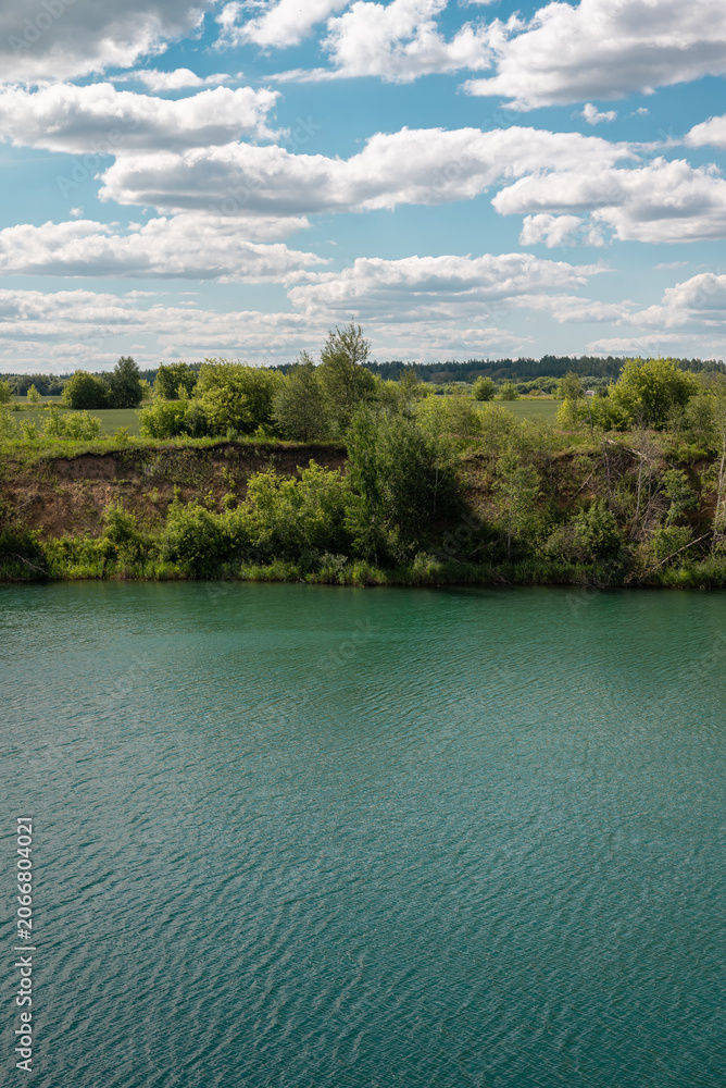 Fototapeta premium Turquoise Lake and Green Shore Under Dramatic Summer Clouds