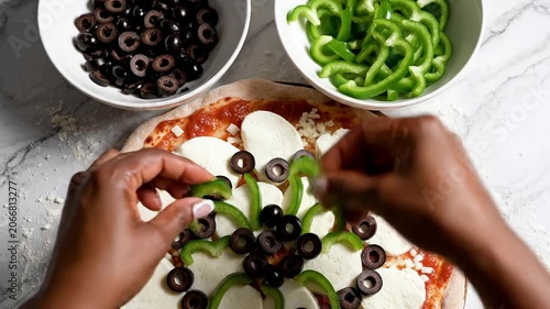 Close-Up Perspective Of Hands Placing Sliced Black Olives And Green Bell Peppers Onto A Freshly Prepared Pizza