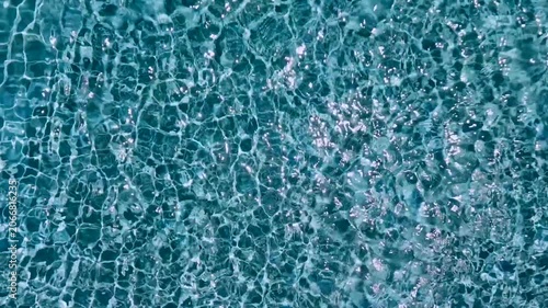 Full frame overhead view of crystal clear turquoise swimming pool water with bright sparkling sun glares and ripples
