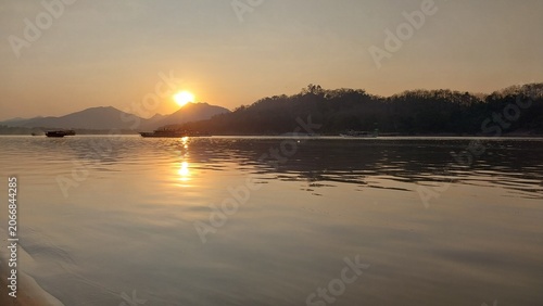 Cuadro en lienzo Serene sunset over a calm river, reflecting warm hues with silhouettes of distant mountains