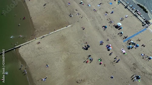 People walk, swim, and relax on Colwyn Bay Beach in the UK. Beachgoers engage in different activities, making the most of the sunny weather. Many families enjoy time together