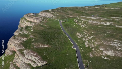 The winding road on the cliffs in Llandudno. You can see the sea below and the landscape along the cliffs. Cars are parked nearby as people enjoy the view