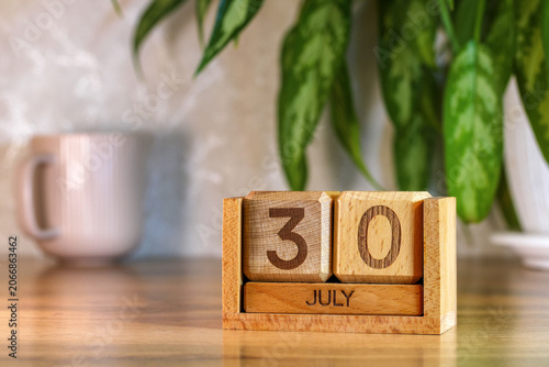 Photos Wooden perpetual calendar showing 30 July with pink mug and houseplant on desk