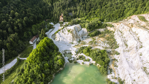 Aerial view of Kamnolom Plese pri Skofljici quarry with a turquoise lake, steep white limestone cliffs, and dense forest in Mali Vrh pri Smarju, Grosuplje, Slovenia.