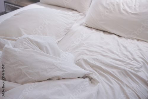 Soft white cotton bedding and rumpled pillows in a messy bedroom offer morning comfort and relaxation. Suitable for lifestyle blogs and interior design websites.