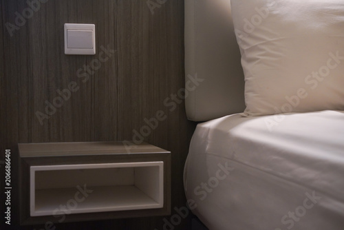 White pillow wooden wall nightstand bedroom furniture light switch modern guest room. Suitable for interior design blogs, home decor magazines, furniture advertisements, and hospitality brochures.