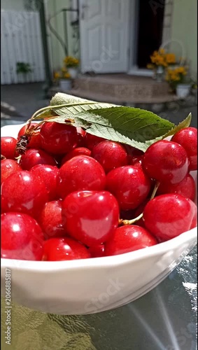Close-up of a female hand picking a ripe red cherry from a bowl filled with fresh summer fruit. Healthy eating concept featuring natural ingredients, freshness and seasonal nutrition.