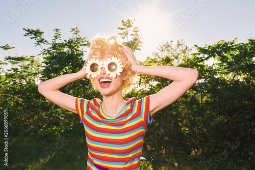Canvas-taulu Smiling woman outdoors wearing a bright striped shirt and playful flower sunglas