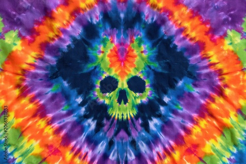 Neon skull symbol in a vibrant tiedye pattern with purple, blue, orange, green, and yellow psychedelic textile texture.